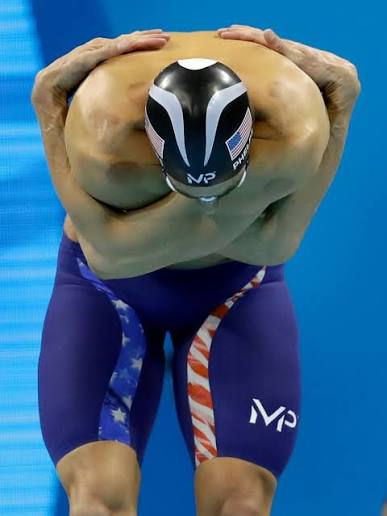 Michael Phelps with arms crossed and reaching behind his head, showing extreme shoulder flexibility with cupping marks